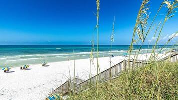 A beach with a wooden boardwalk, beach umbrellas, and tall grasses.