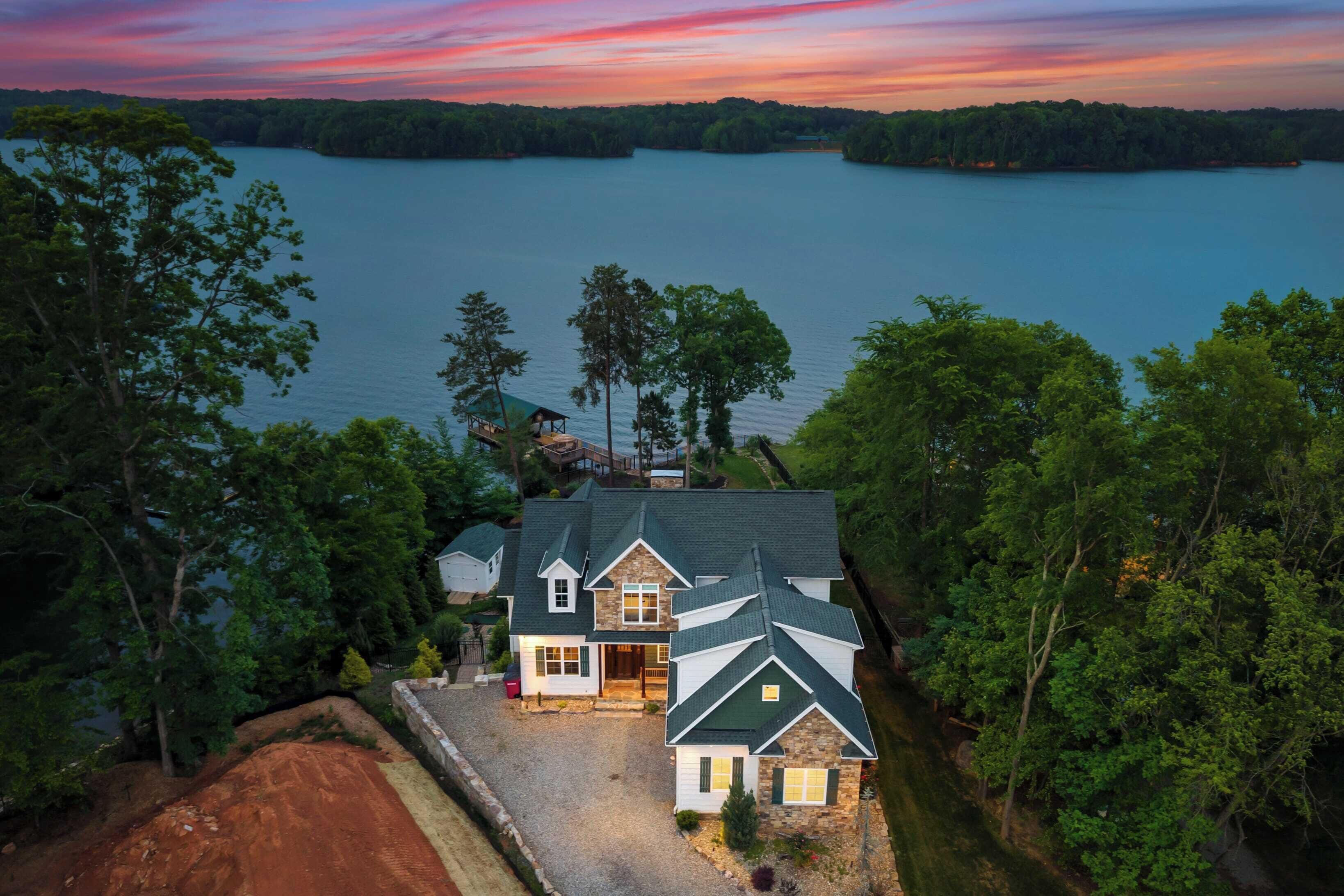 A large house with a stone facade, a green roof, and a driveway leading to a dock.