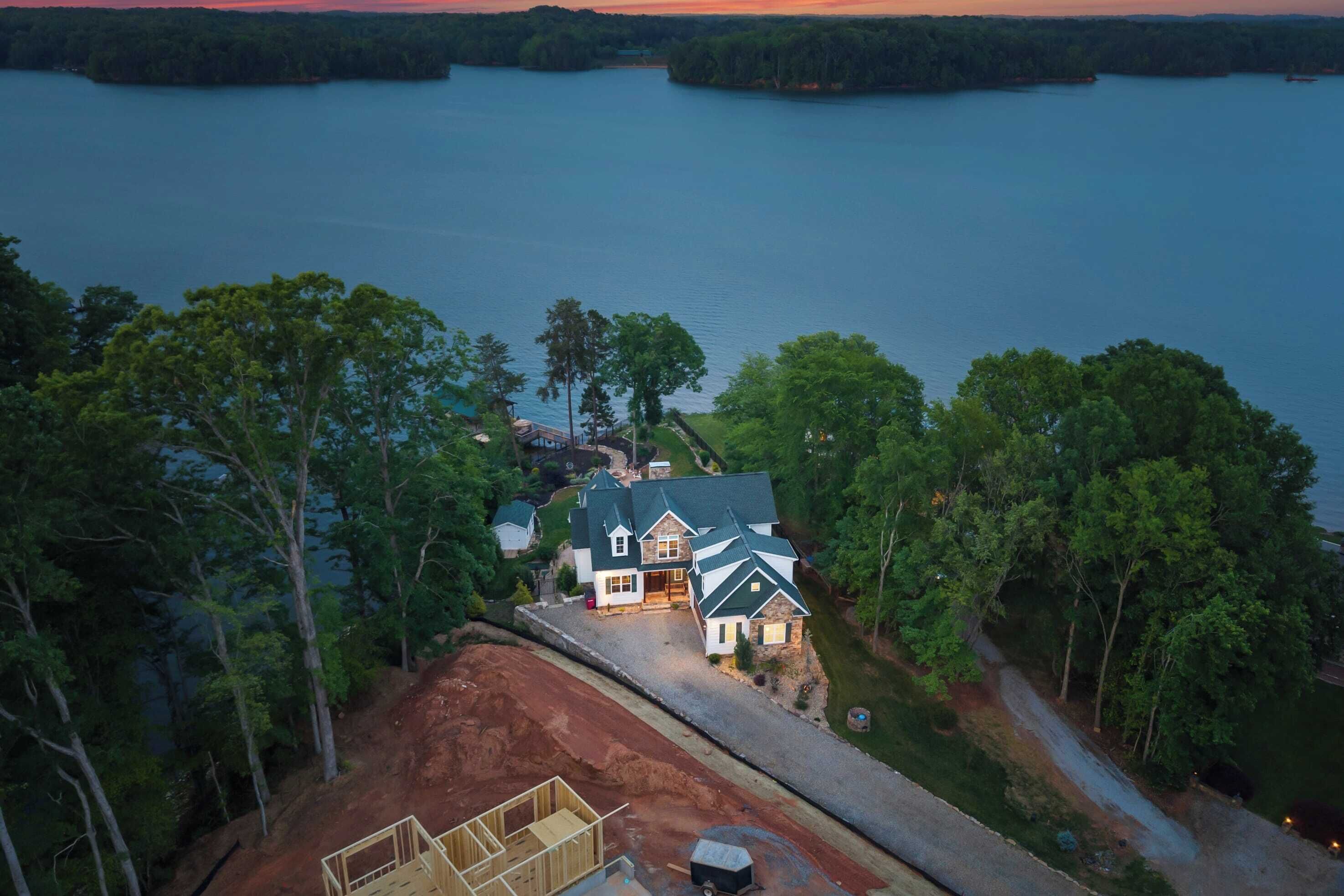 Una casa grande con techo verde y múltiples chimeneas, rodeada de árboles y un lago.