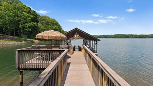 A wooden pier leading to a covered area with a thatched roof, overlooking a calm lake and surrounded by trees. - Spacious Waterfront Home on Lake Norman With Firepit, Views, and Dock Access (Sherrills Ford)