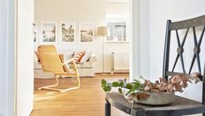 A living room with a wicker chair, a sofa, and a coffee table with a plant. There are framed pictures on the wall and a lamp. - Holiday Home in Terherne Near Scenic Friesland (Terherne)