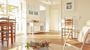 A bright room with wooden flooring, a white desk, wicker chairs, and a glass coffee table with decorative items. - Holiday Home in Terherne Near Scenic Friesland (Terherne)