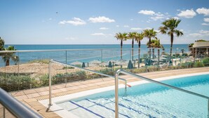 A pool area with a view of the sea, lounge chairs, and palm trees.