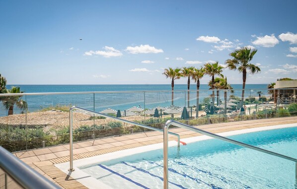 A pool area with a view of the sea, lounge chairs, and palm trees.