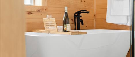 Une salle de bain rustique, avec des murs en bois, une baignoire blanche, une bouteille de vin et un porte-serviettes.