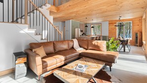 A modern living room with a brown leather sectional sofa, a wooden coffee table, and a staircase with wooden railings. - Chamonix Kanata Tremblant (140 Pavillon-Kanata) (Amherst)