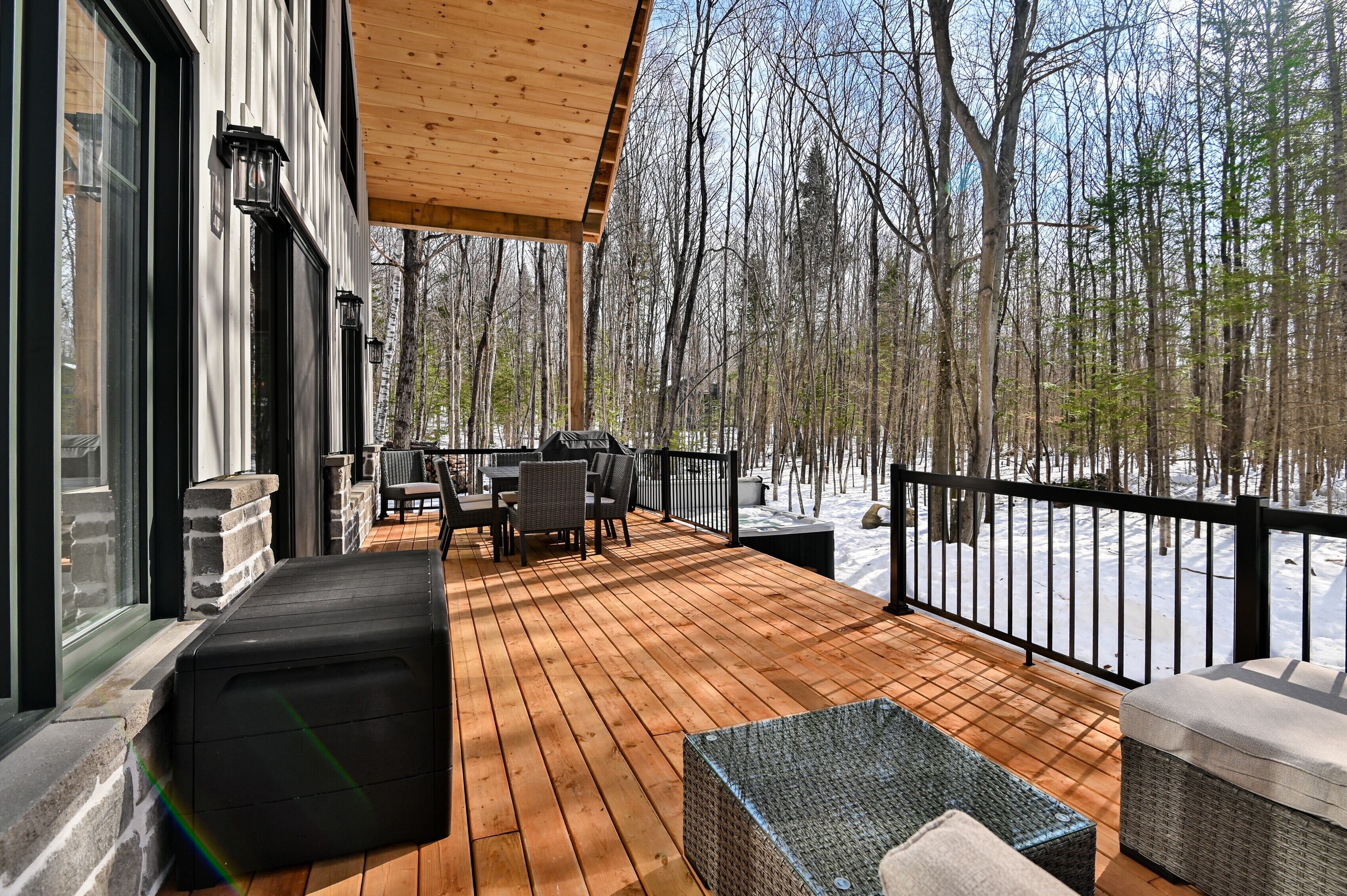 A wooden deck with outdoor furniture, a railing, and a view of a snowy forest.