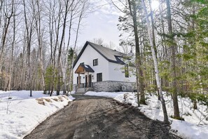 A white building with a stone foundation, surrounded by snow-covered ground and trees. - Chamonix Kanata Tremblant (140 Pavillon-Kanata) (Amherst)