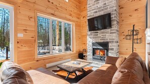 A cozy cabin interior with a stone fireplace, wooden walls, and a large window overlooking a snowy landscape. - Chamonix Kanata Tremblant (140 Pavillon-Kanata) (Amherst)