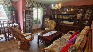 Una sala de estar acogedora con una mesa de centro de madera, un sofá estampado y una estantería llena de libros y objetos decorativos.