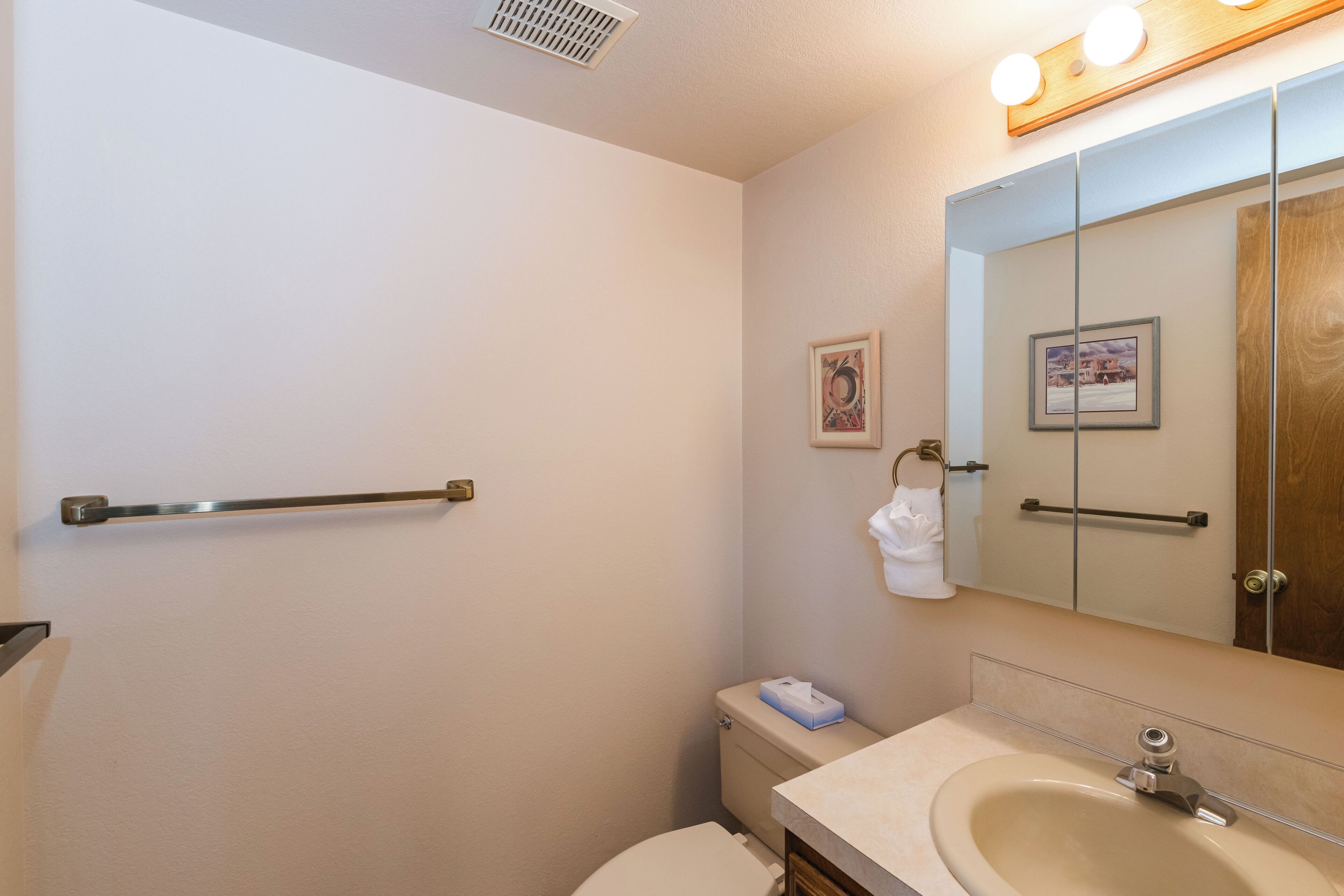 Une salle de bain équipée de toilettes, d’un lavabo et d’un miroir avec une porte en bois. Il y a une main courante sur le mur et un cadre photo accroché au mur.