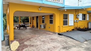 Un edificio amarillo con un porche techado, una mesa y un ventilador.