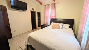 Un dormitorio con cama, televisor montado en la pared, mesita de noche, armario y puerta.