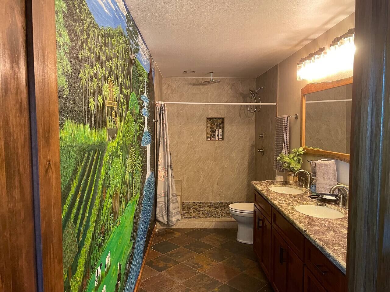 Casa de banho com chuveiro, duas pias, espelho e um mural decorativo.