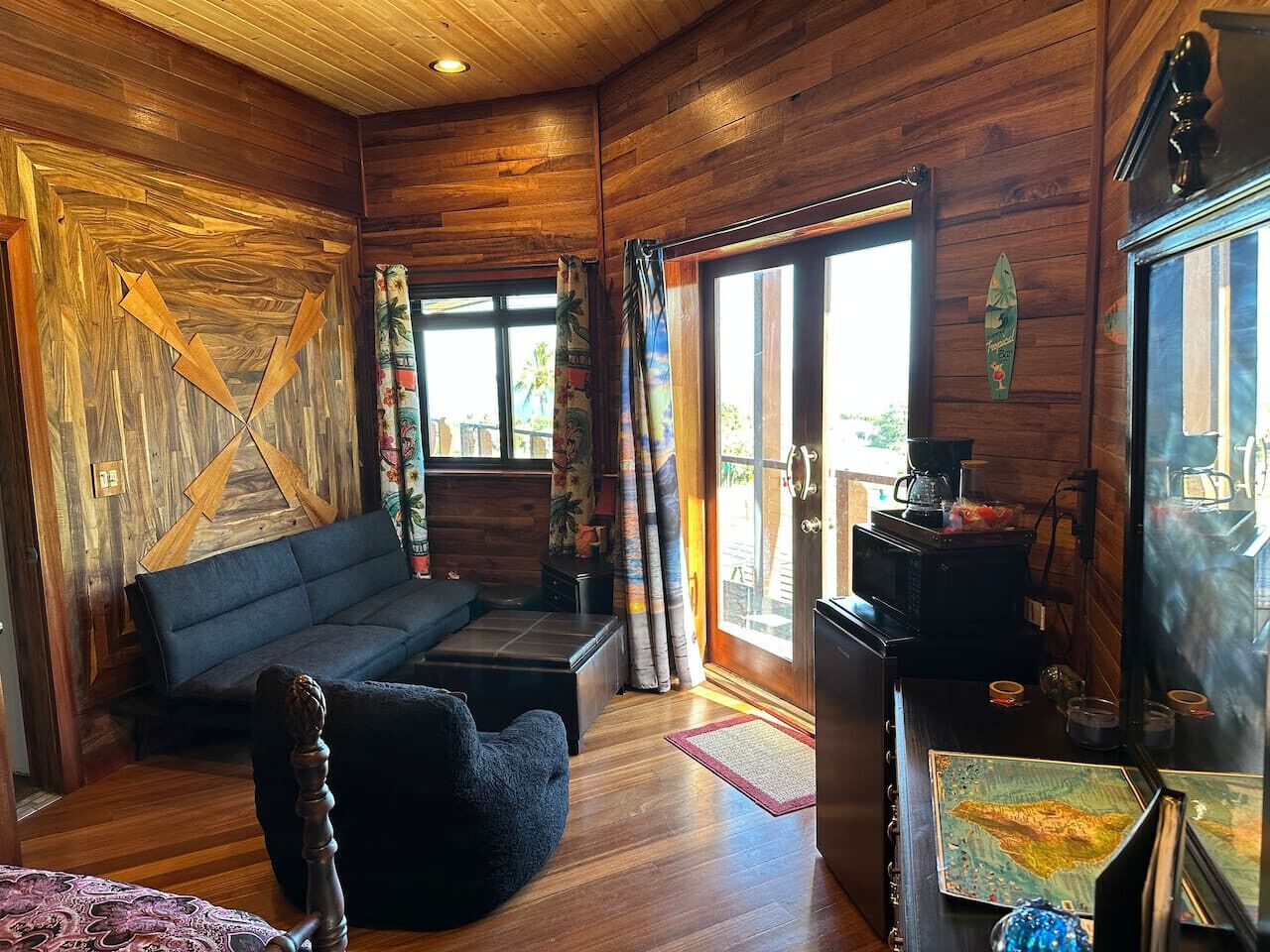 A cozy cabin interior with a wooden interior, a sofa, a chair, a coffee table, and a kitchen area with a stove.