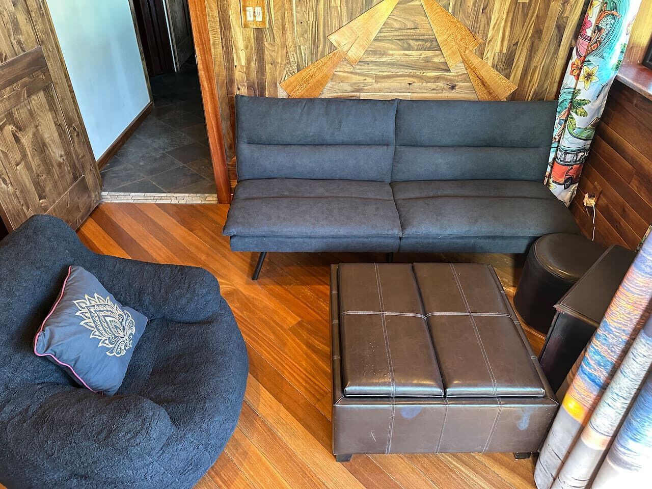 Quarto com um sofá azul escuro, um banquinho combinando e uma poltrona de bean bag azul escuro com uma almofada decorativa.