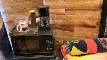 Ett litet kök med mikrovågsugn, kaffebryggare och förvaringsbehållare. Det finns en väggpanel av trä med en skylt som visar ordet ”Sommar” och en surfbräda som dekoration.