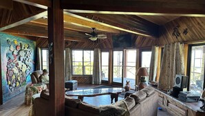 A spacious living room with a large wooden ceiling, a fireplace, a sofa, and a dog. - Magic Skies Surfs Up Room (Hilo)