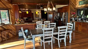 A spacious kitchen with wooden cabinets, a dining area with white chairs, and a large island with a sink. - Magic Skies Koi Pond View Handicap Accessible Room (Hilo)