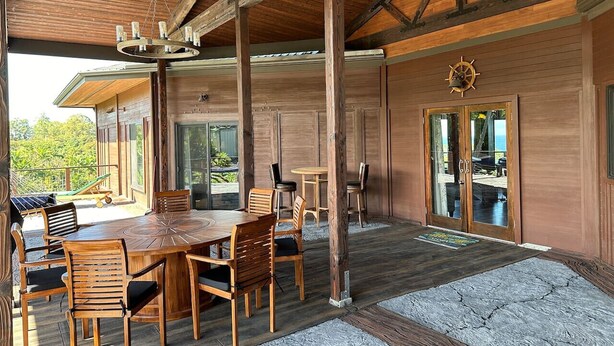 A wooden dining area with a large round table and chairs, a wooden ceiling with exposed beams, and a view of the outdoors. - Magic Skies Koi Pond View Handicap Accessible Room (Hilo)