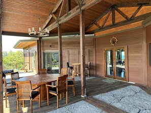A wooden dining area with a large round table and chairs, a wooden ceiling with exposed beams, and a view of the outdoors. - Magic Skies Koi Pond View Handicap Accessible Room (Hilo)