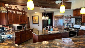 A kitchen with granite countertops, wooden cabinets, and pendant lighting. - Magic Skies Koi Pond View Handicap Accessible Room (Hilo)