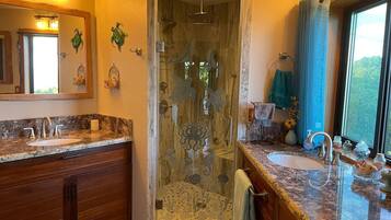 A bathroom with a glass-enclosed shower, a vanity with a sink, and a large mirror.