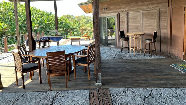 An outdoor patio area with a round table and chairs, a hammock, and a wooden deck.