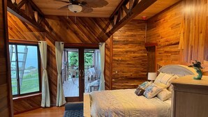 A wooden cabin bedroom with a bed, a bench, and a view of the outdoors.