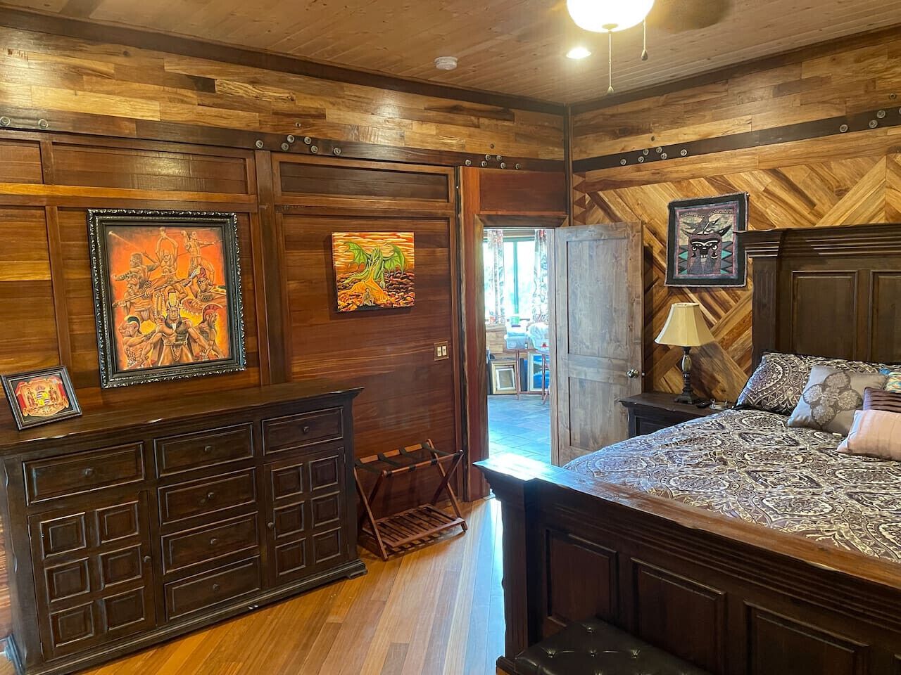A wooden-paneled room with a bed, dresser, and artwork.