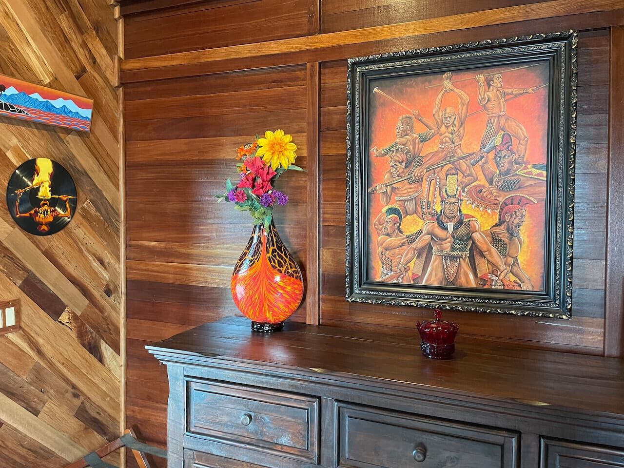 Una pared de madera con un cuadro enmarcado, un jarrón con flores y un plato decorativo.