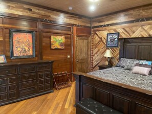 A bedroom with a large bed, wooden paneling, and artwork on the walls. - Magic Skies Hawaiian Kingdom Hula Room (Hilo)