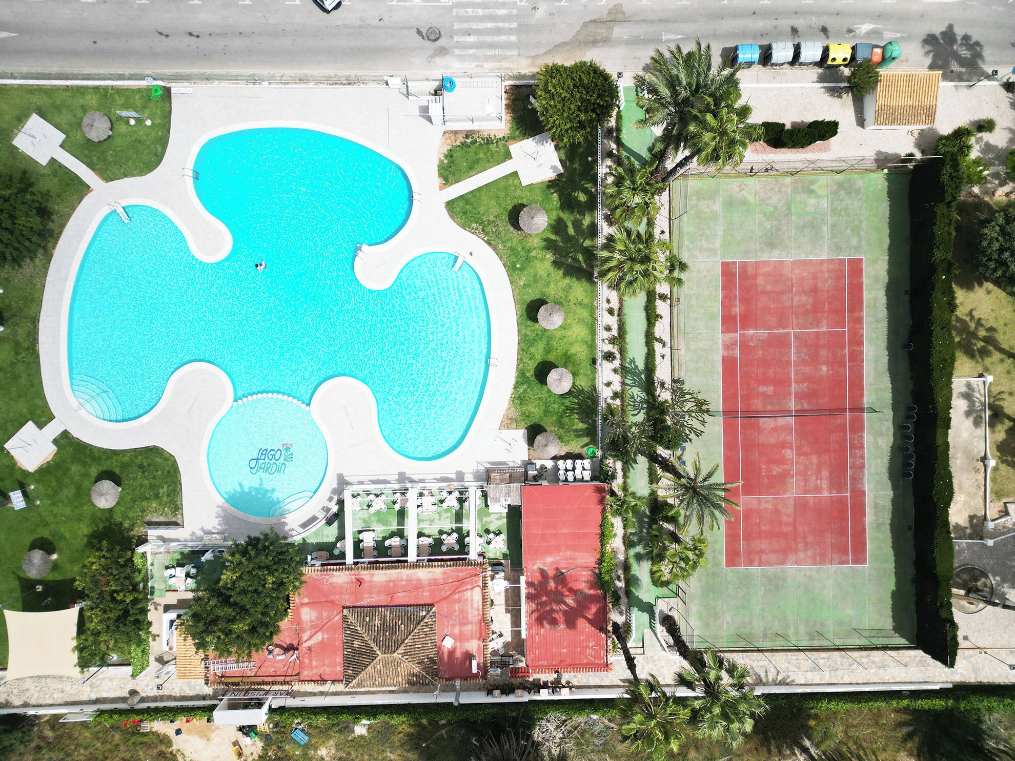 Eine Vogelperspektive eines Erholungsgebiets mit einem großen, blauen Pool, einem Tennisplatz und umgebender Bepflanzung.