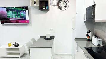 A modern kitchen with a built-in oven, a coffee machine, and a TV displaying flight information.