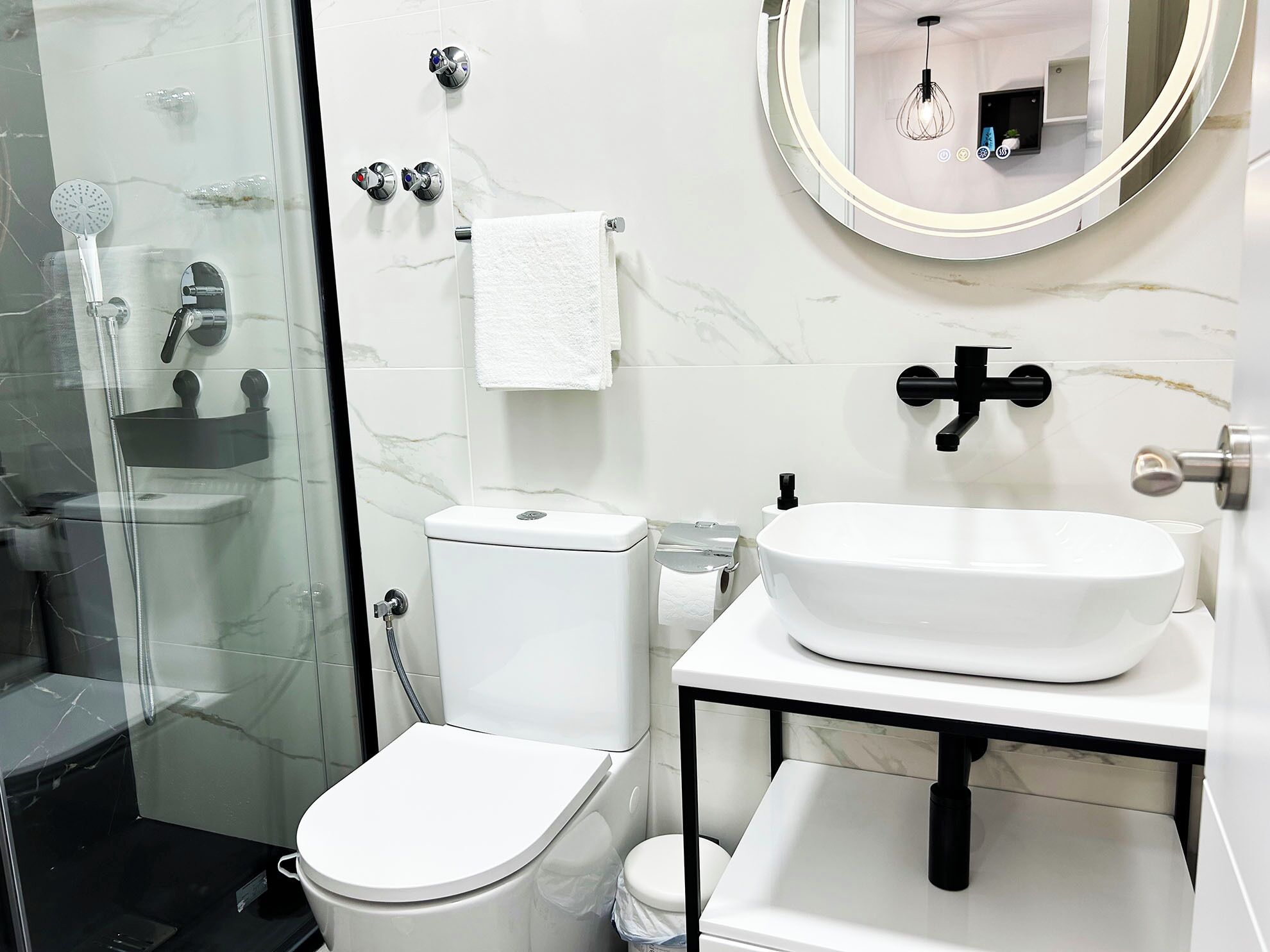 A modern bathroom with a glass shower enclosure, a toilet, a sink with a mirror above it, and a towel hanging on the wall.