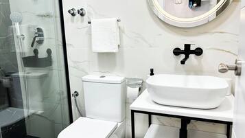 Un baño moderno con cabina de ducha de vidrio, inodoro, lavabo con espejo y una toalla colgada en la pared.