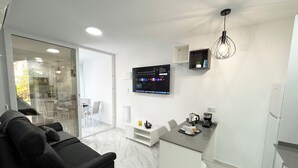 A modern living room with a black sofa, a small kitchen area with a coffee maker, and a TV mounted on the wall. - Bungalow by the pool with 2 terraces, maximum capacity for 4 people (Torrevieja)