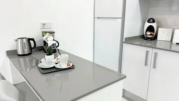 A modern kitchen with a refrigerator, coffee maker, kettle, and a tray with cups and a flower.
