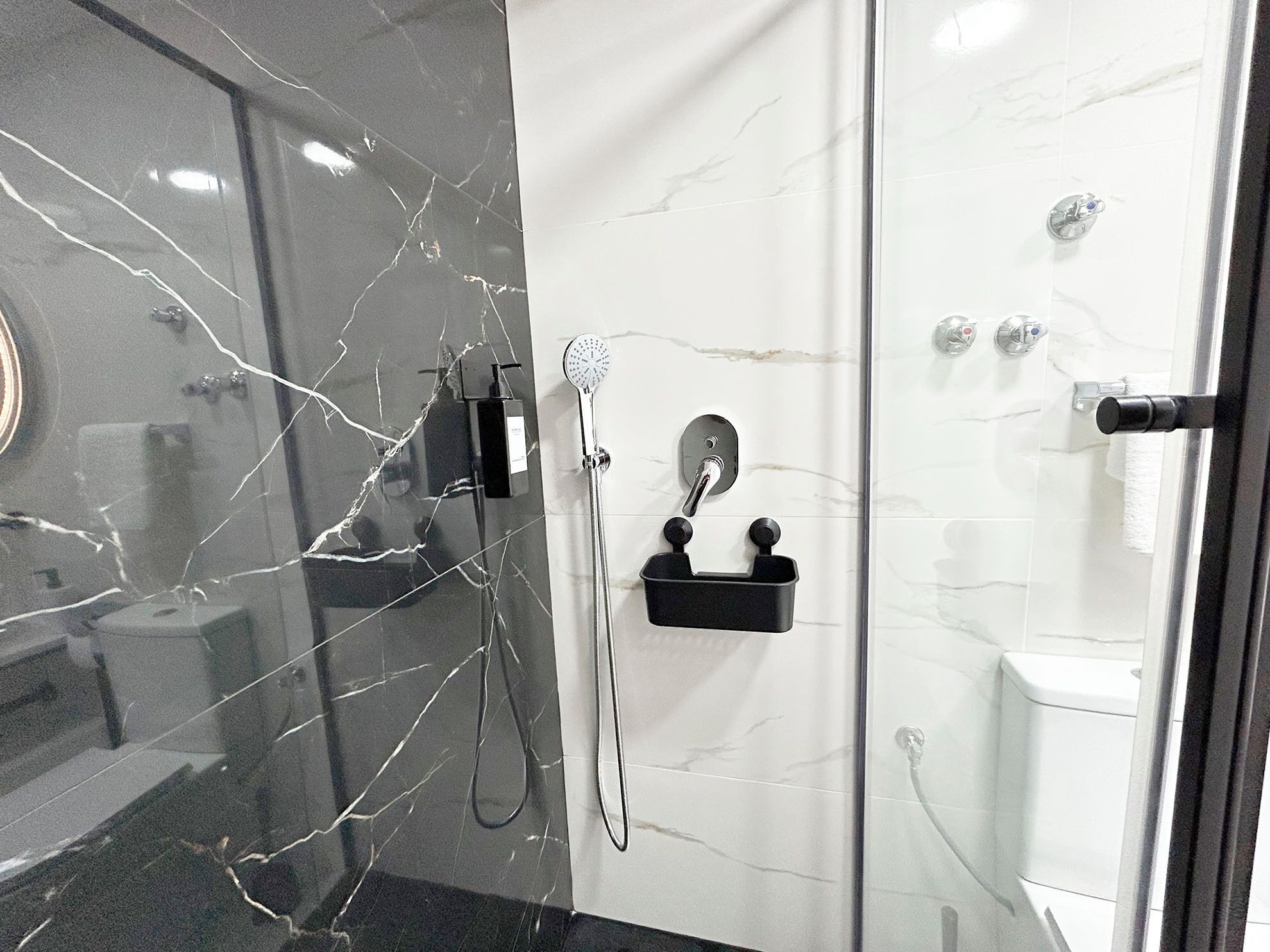 A modern bathroom with a glass shower enclosure, marble walls, and a black soap dish.