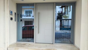 A building entrance with a glass door, a red car parked outside, and a balcony with a railing. - Comfort Holidays (Messini)