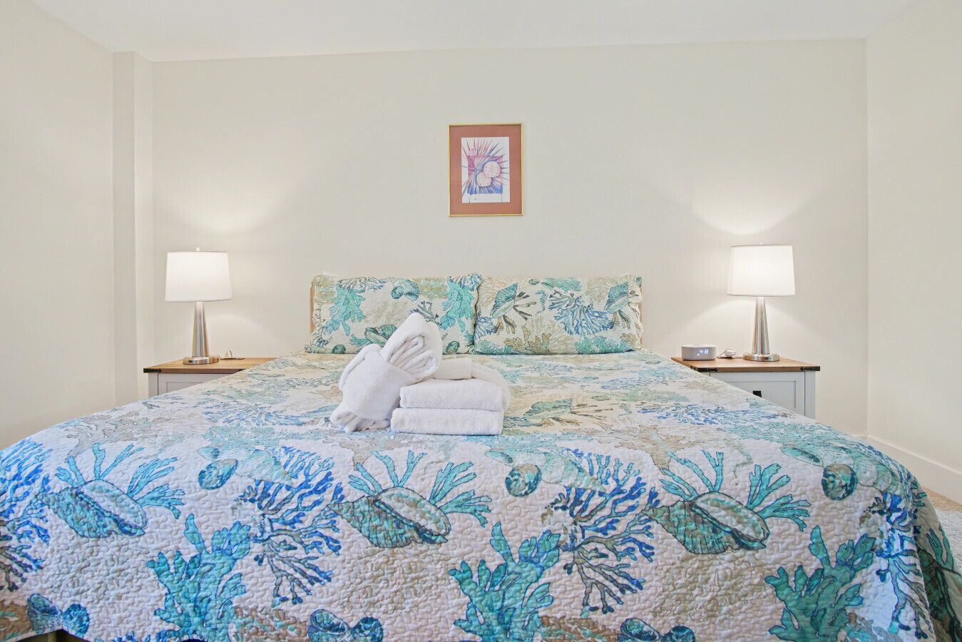 A hotel room with a bed, two bedside lamps, a framed picture on the wall, and a floral bedspread.