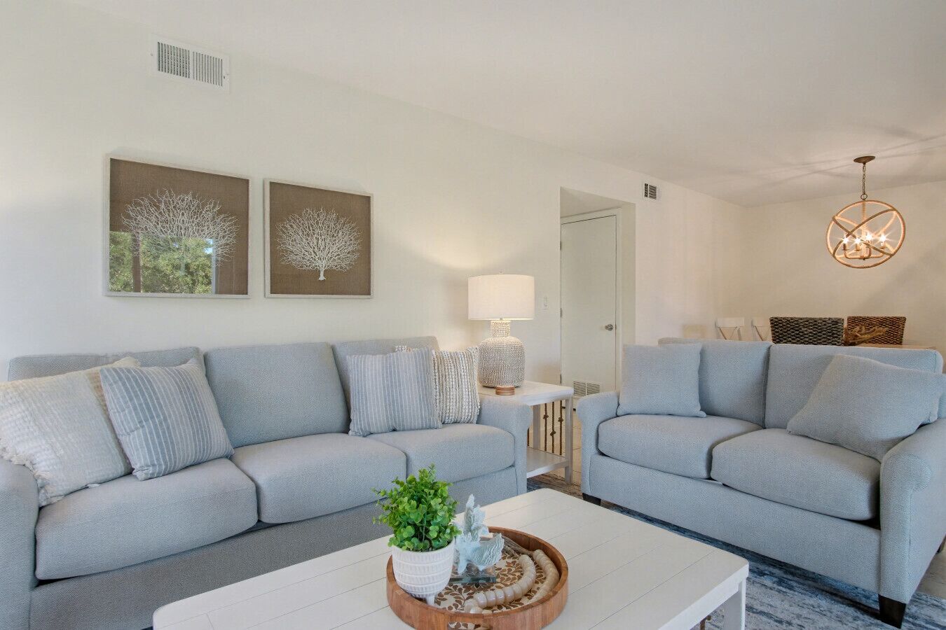 A modern living room with two grey sofas, a white coffee table with decorative items, a floor lamp, and wall art.