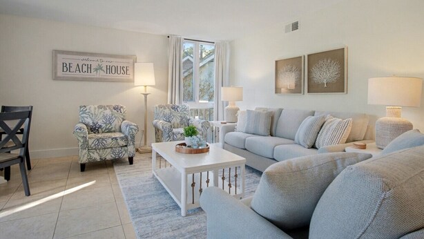 Un salon avec un canapé blanc, deux fauteuils à motifs, une table basse et un tableau encadré accroché au mur.