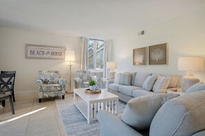 Ein Wohnzimmer mit einem weißen Sofa, zwei gemusterten Sesseln, einem Couchtisch und einem gerahmten Schild an der Wand.