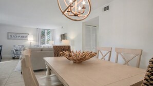 Un coin repas avec une table en bois, des chaises et une pièce maîtresse décorative. On aperçoit un canapé et une lampe au fond.