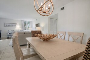 A dining area with a wooden table, chairs, and a centerpiece. There is a sofa and a lamp in the background. - Updated 3BR Sea Pines-New Furnishings-Sleeps 8-Pool - 887 Ketch Court (Hilton Head Island)