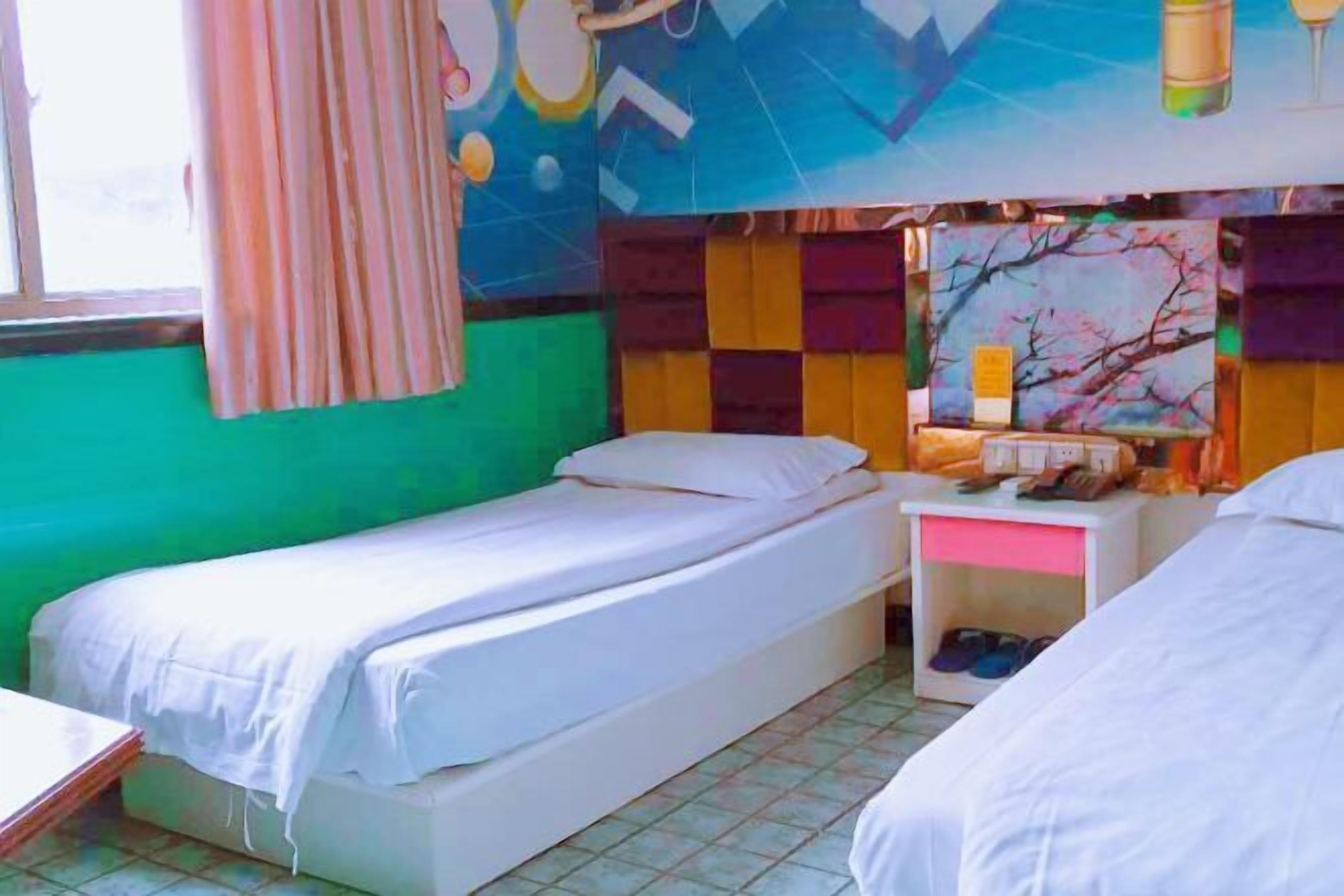 A room with two single beds, a small table, and a nightstand with a lamp.