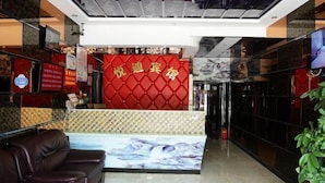 A reception area with a red wall and a large screen displaying a landscape. There is a brown leather sofa and a plant to the right. - Yuedi Hotel (Shanghai)