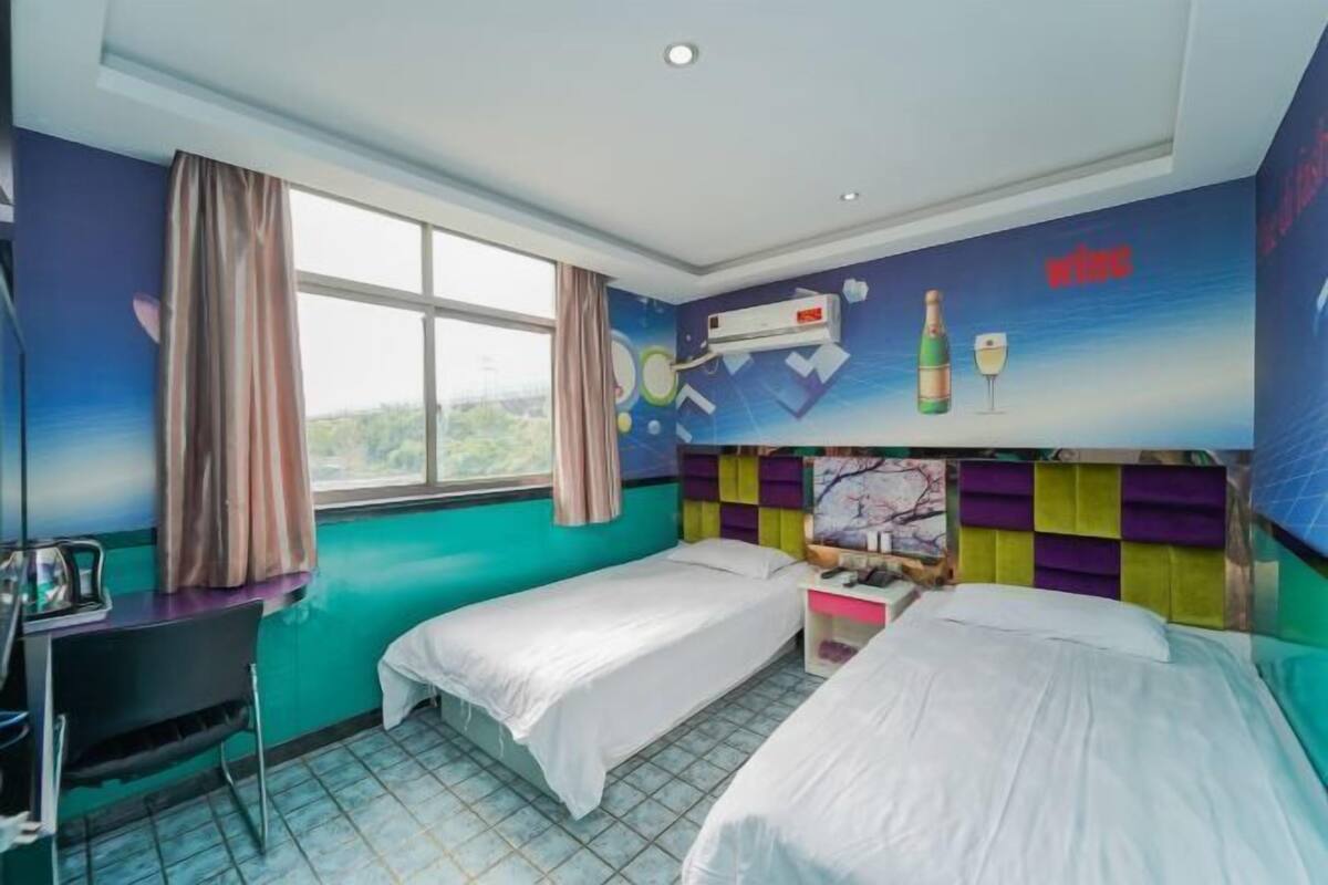 A room with two beds, a desk, and a window with curtains.