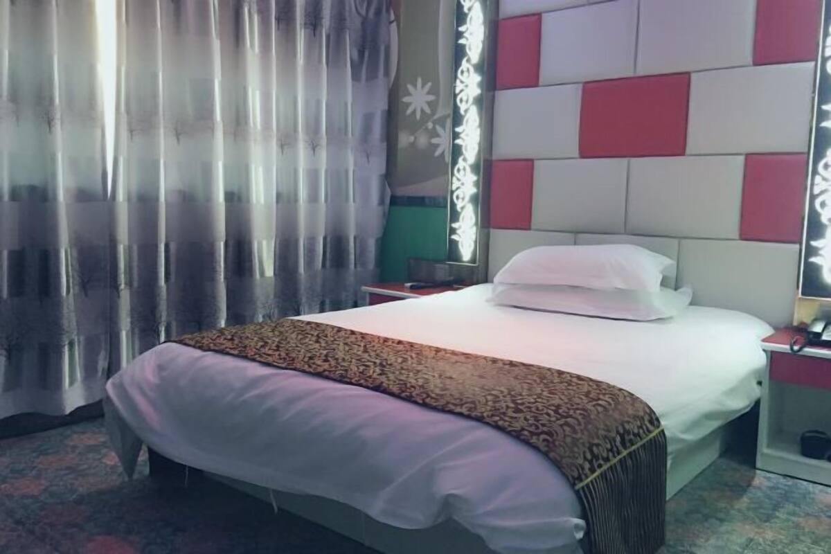 A hotel room with a bed, curtains, a bedside table, and a wall with a geometric pattern.